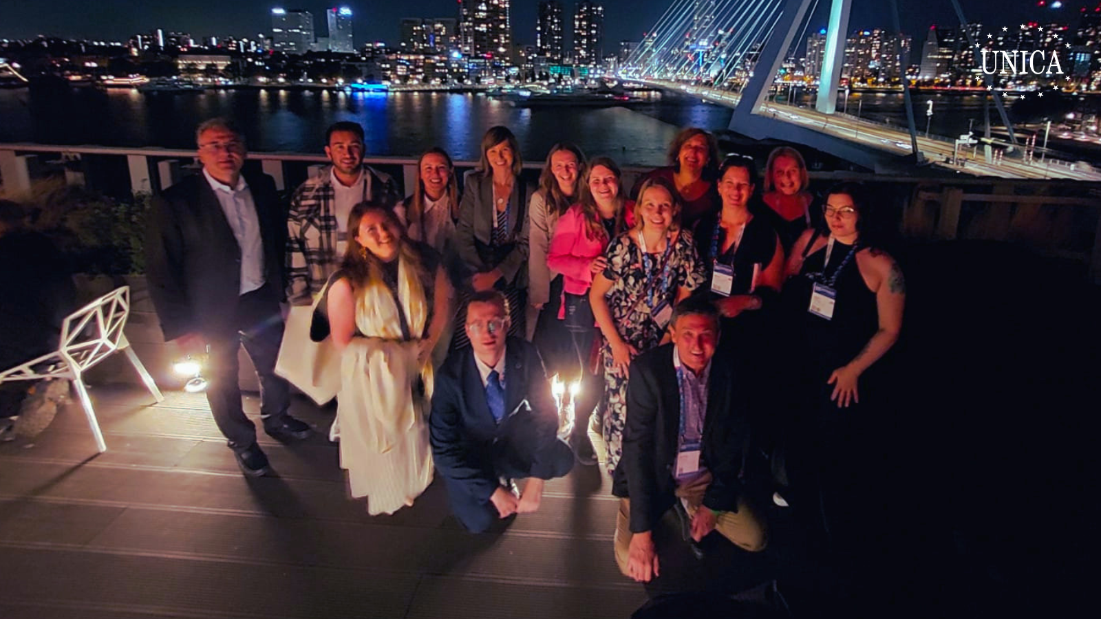 Group of 14 people posing for a picture at night with the Erasmus bridge in Rotterdam in the background