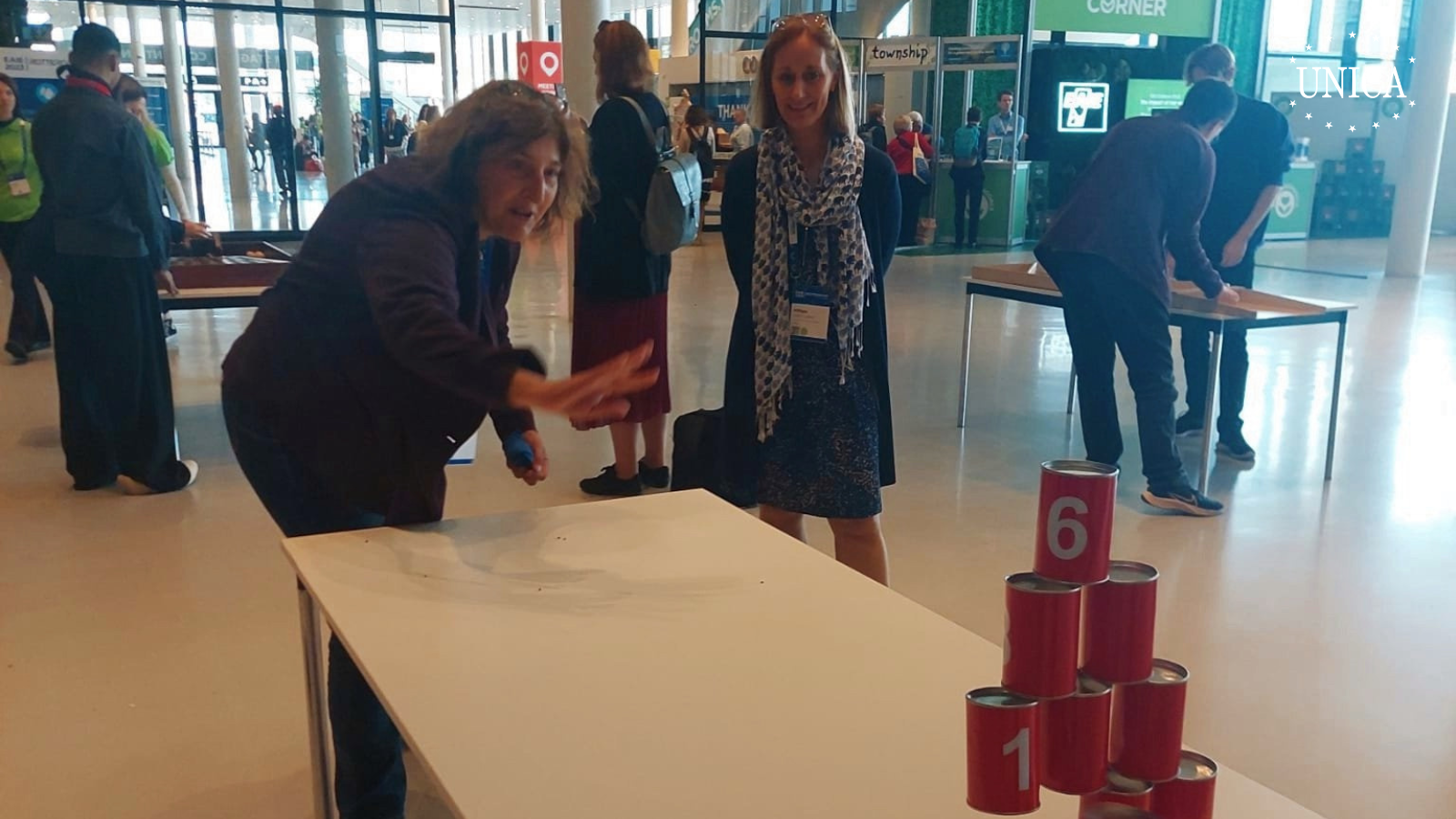 Woman playing a traditional game similar to bowling with stacked cans and a bag of sand